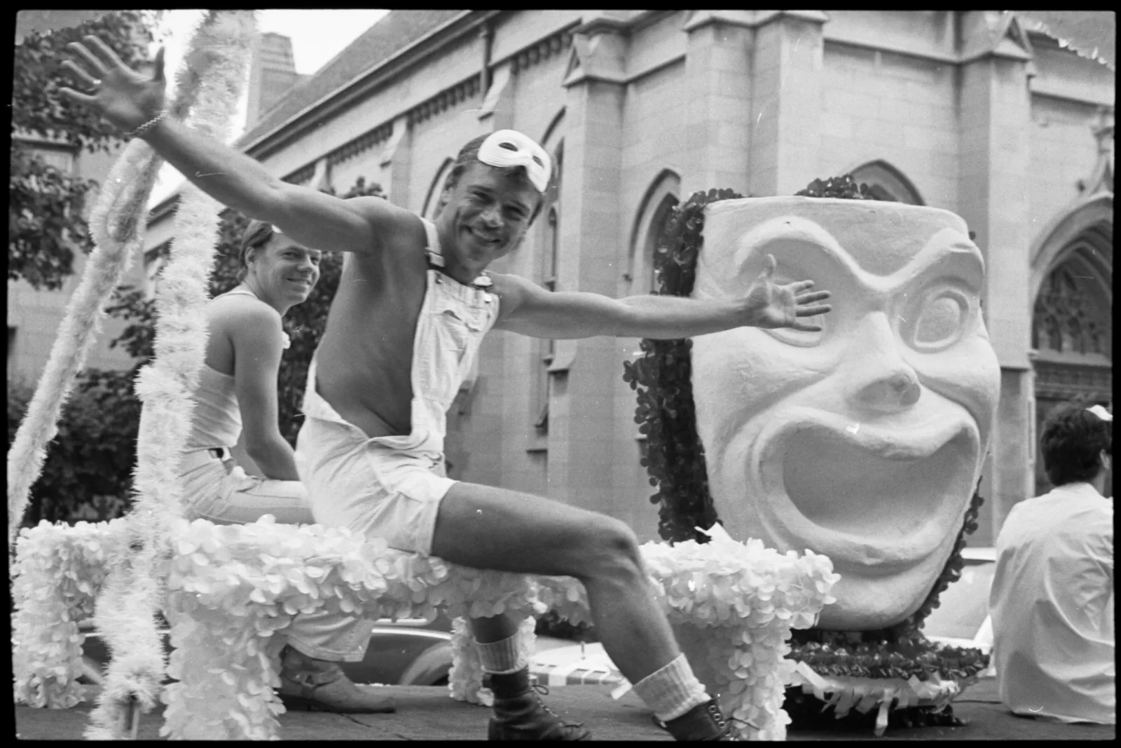 Midwest ms militante box 001 fl 004 008 Two men dressed in white sit on a float in the parade. The float has a big mask on it.